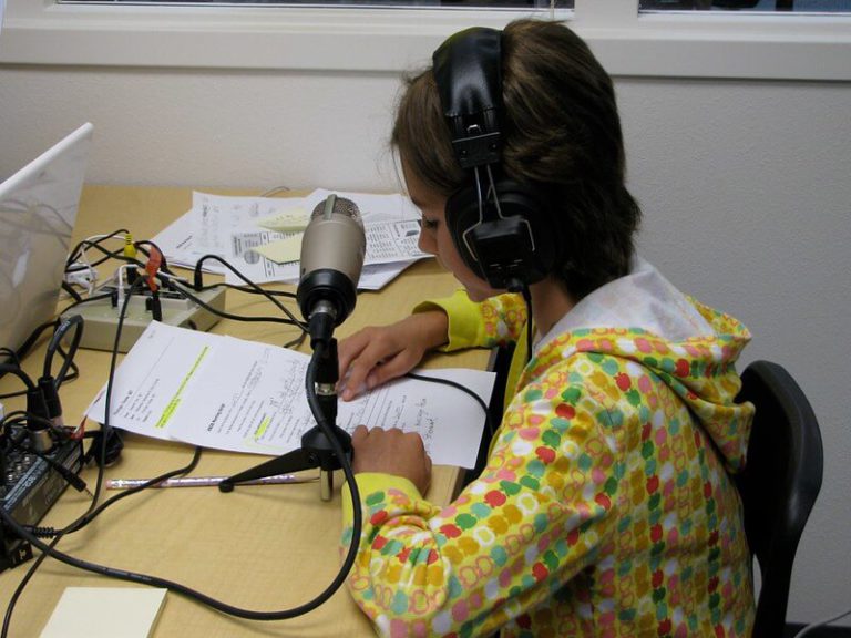 A student records her script into a microphone to be used as part of an educational podcast.