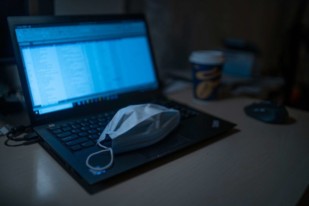 A COVID-19 mask is taken off as an employee is working from home on a laptop